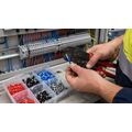 Electrician crimping colour-coded bootlace ferrules onto stranded wire at a switchboard panel in an Australian commercial installation.